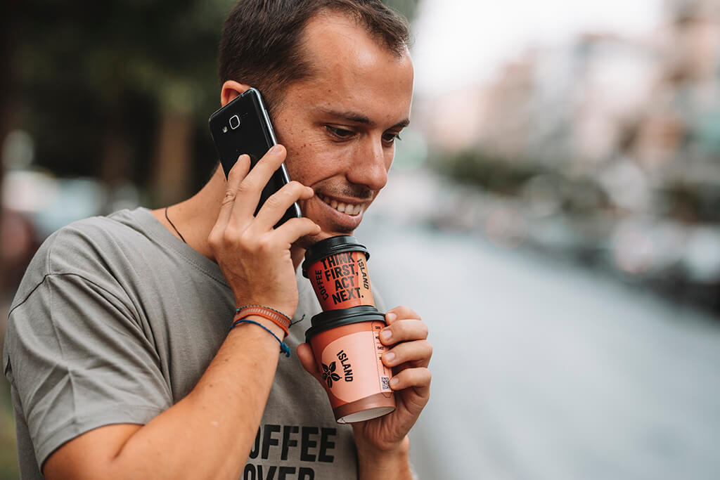 Man speaking on the phone while holding two paper cup coffees