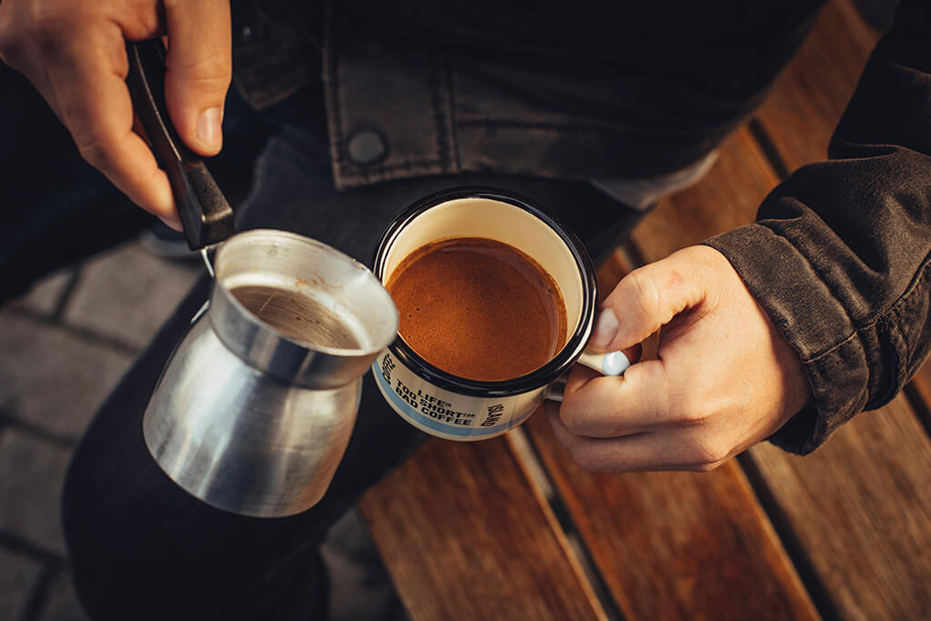 A man pouring ibrik coffee in a mug.