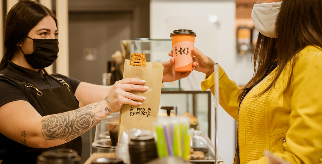 COFFEE ISLAND'S BARISTA OFFERING FOOD AND COFFEE TO A CUSTOMER.